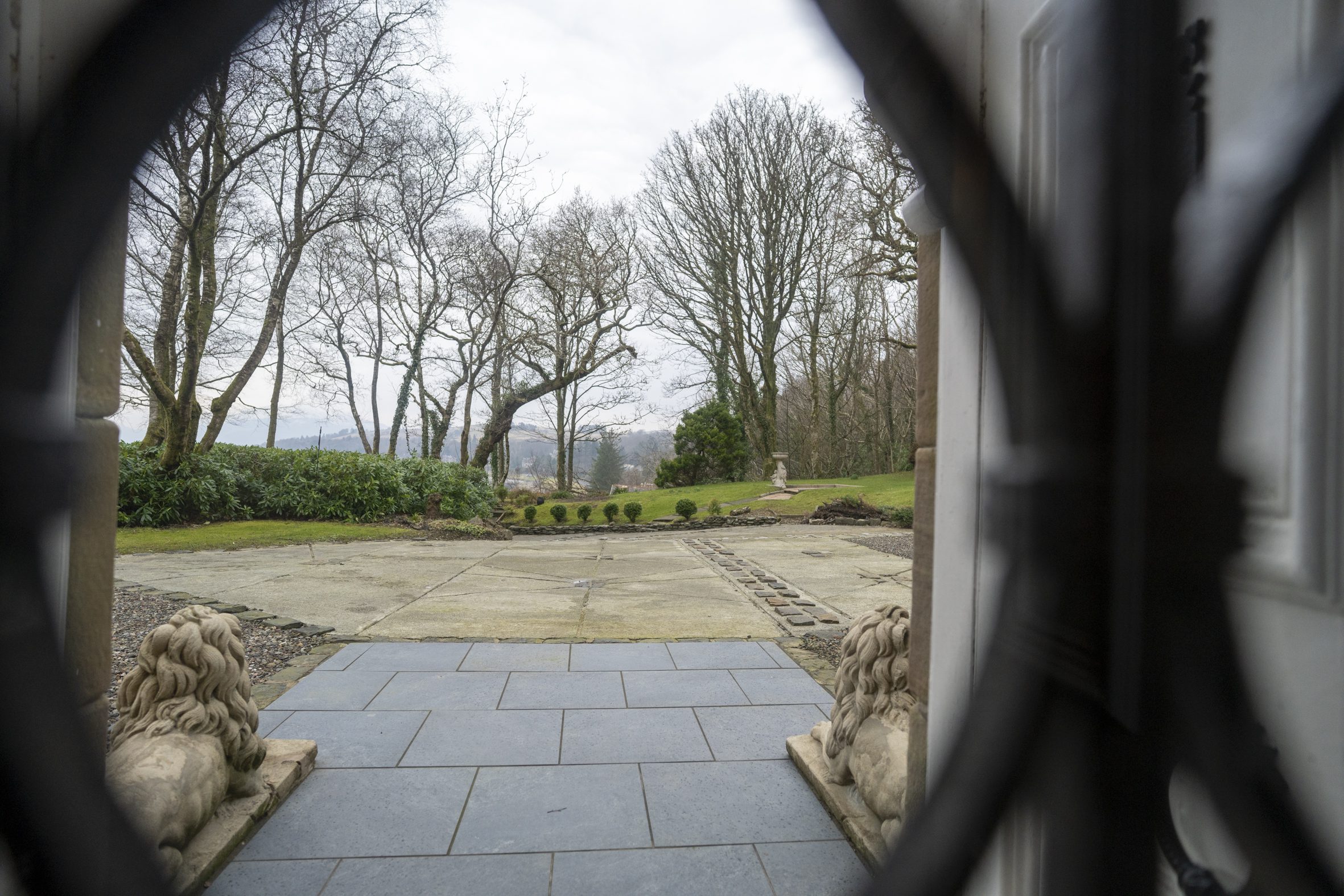 View from a doorway looking out onto a landscaped garden with bare trees in the background and a stone lion sculpture in the foreground.