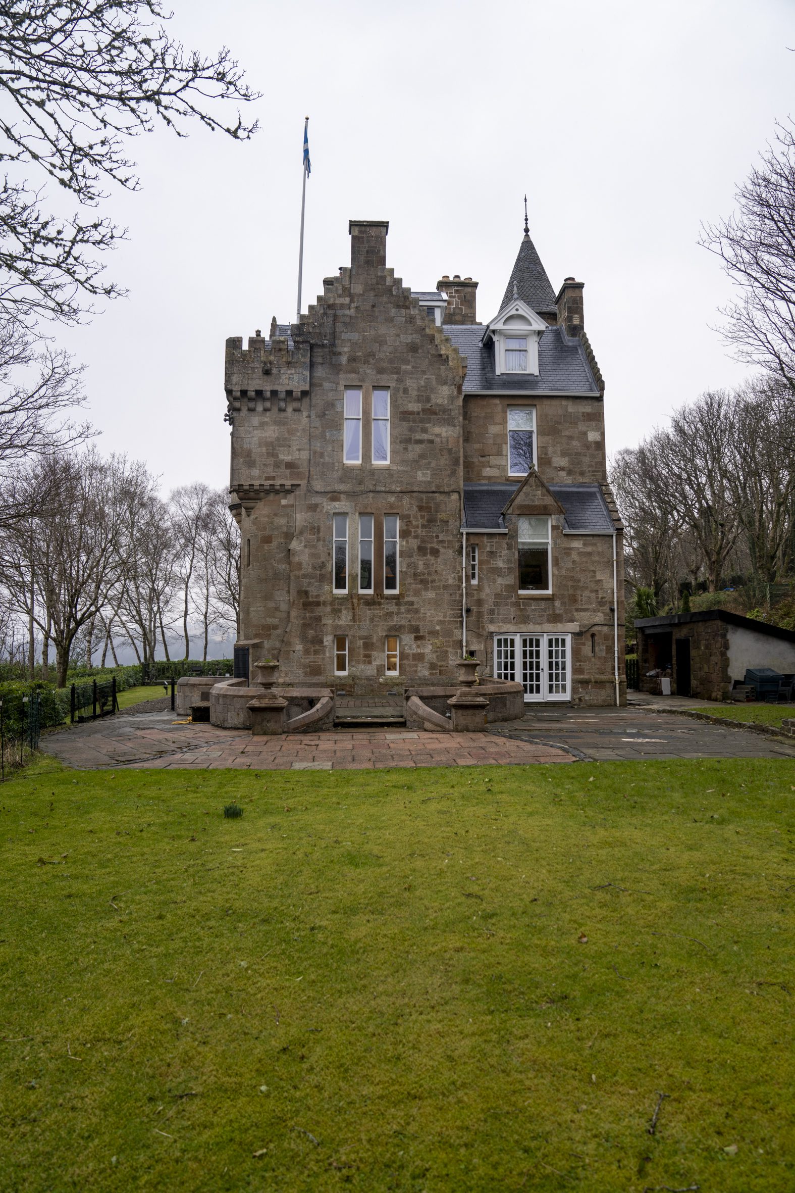 Exterior view of a stone castle with a flag, surrounded by green grass and trees, located in Scotland.